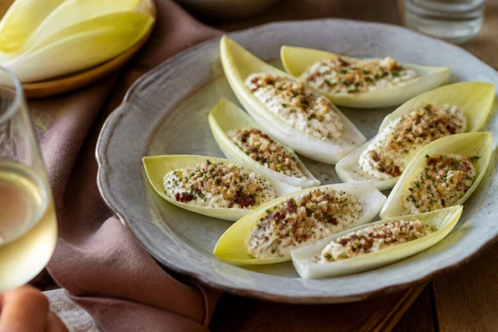 Feuilles d'endives farcies pour l'apéritif, garnies de roquefort aux noix, saumon fumé, avocat crevettes, tapenade chèvre et feta betterave, dressées sur un plateau en bois