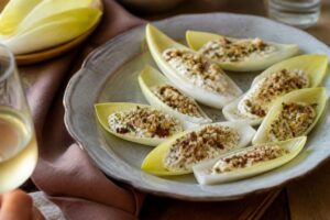 Feuilles d'endives farcies pour l'apéritif, garnies de roquefort aux noix, saumon fumé, avocat crevettes, tapenade chèvre et feta betterave, dressées sur un plateau en bois