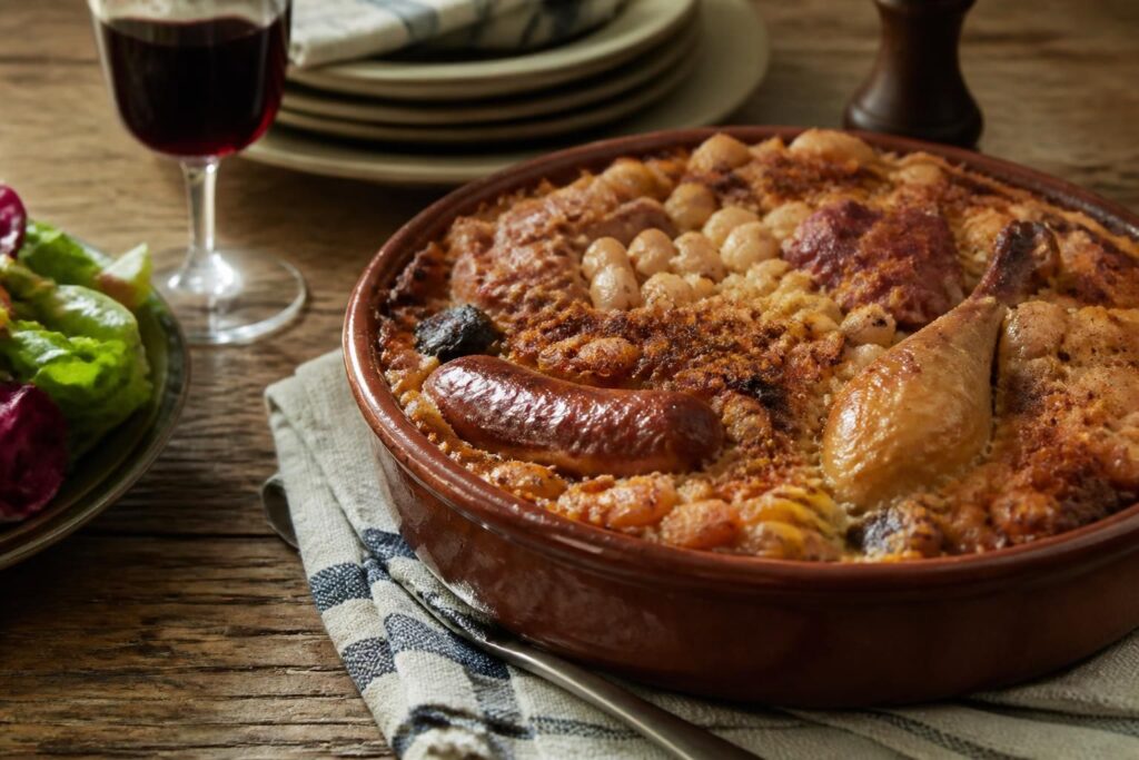 Cassoulet maison de grand-mère dans une cassole en terre cuite, croûte dorée et saucisse de Toulouse apparente, servi sur une table rustique en bois