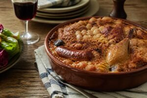 Cassoulet maison de grand-mère dans une cassole en terre cuite, croûte dorée et saucisse de Toulouse apparente, servi sur une table rustique en bois